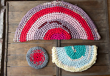 Three rugs sitting on a wooden base, two folded in half and one small circular one unfolded.