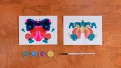 Two images of Rorschach-stye ink blog paintings plus four cakes of metallic watercolor and a watercolor brush.