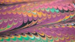 A close-up image of a piece of hand-made marbled paper in green, purple, pink and black,