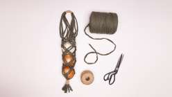 An overhead image of a rope bag holding onions, a spool of T-Shirt yarn, a spool of twine, and a pair of scissors from Cobrina's Knotted Pantry Bag Creativebug class.