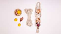 An overhead image of a string-bag holding fruit, a bundle of cotton strings, and lemons from Cobrina's Knotted Pantry Bag Creativebug class.