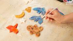 A hand painting details on a gingerbread man salt dough ornaments.