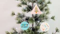 Three ornaments from Faheema Chaudry's Make Ornaments with Polymer Clay and Transfers class, hanging on an evergreen tree.
