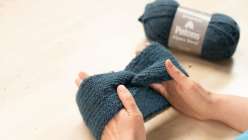 Two hands holding a blue ribbed knit headband and a skein of matching teal yarn.