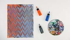 A piece of marbled paper, three marbling inks, and a messy palette from Mercedez Rex's Advanced Marbling Techniques class on Creativebug