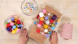 Pom Moms and paper straws being strung together into a garland in Twinkie Chan's Make Celebration Garlands class on Creativebug