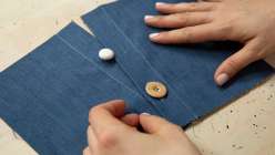 A pair of hands sewing a button onto blue fabric from Amanda Todaro's Garment Sewing: Design Details class on Creativebug.