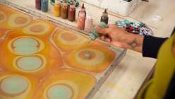 A hand dropping ink onto a tray of water in Mercedez Rex's Marbling Finished Goods class on Creativebug.