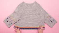 A grey crocheted sweater with colorful bobbles on the sleeves made in Twinkie Chan's Design and Crochet a Top-Down Bobble Sweater class on Creativebug.