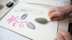 A hand pressing an inked leaf into a piece of paper made by Lorene Edwards Forkner in her Gather and Make: Four Garden Projects class on Creativebug.