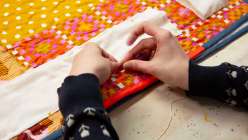 A pair of hands hand stitching a tube of fabric to a decorative quilt in Heidi Parkes's Add a Display Sleeve to a Quilt class on Creativebug