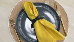 A yellow linen napkin with a bow-shaped leather napkin ring made in the Make Leather Napkin Rings class on Creativebug