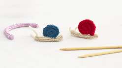 Two I-cord knit snails, a pink I-cord worm, and two knitting needles from Faith Hale's Kids Knitting: I-Cord and Garter Stitch Bugs class on Creativebug. 